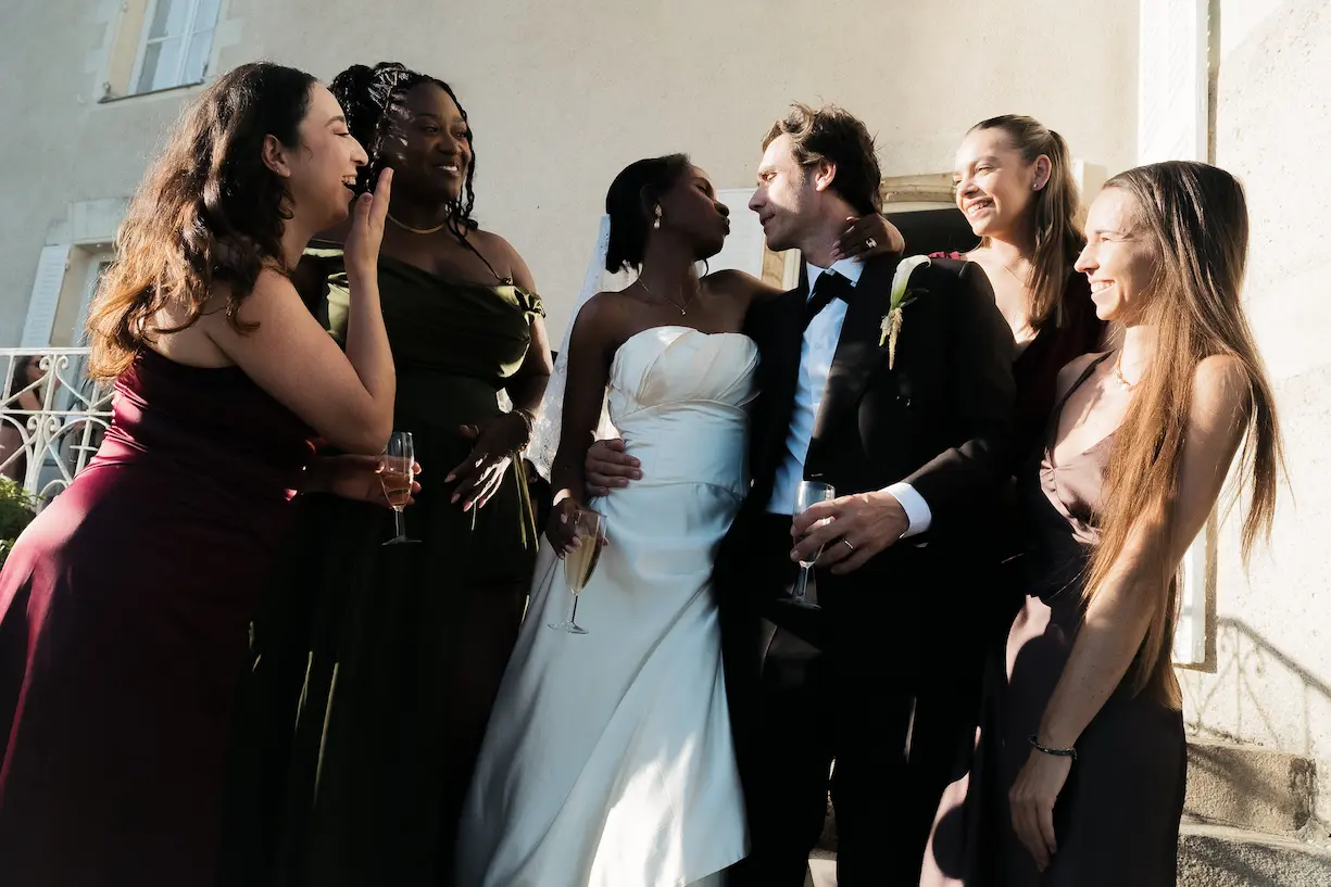 Les marié·es, entouré·es de leurs demoiselles d'honneur, partagent un moment de complicité et de rires lors du cocktail de mariage en extérieur.